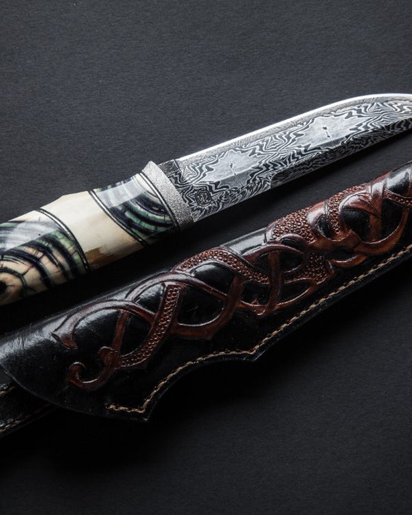 Damascus steel knife with leather sheath on a dark background