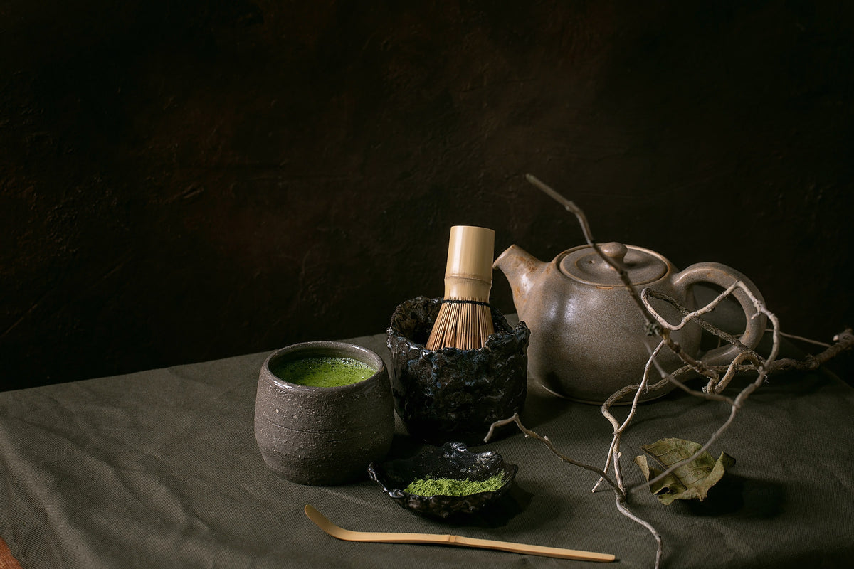 matcha bowl and whisk beside clear glass teapot with green tea, soft morning light on linen, no text no logos