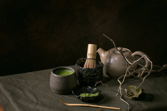 matcha bowl and whisk beside clear glass teapot with green tea, soft morning light on linen, no text no logos