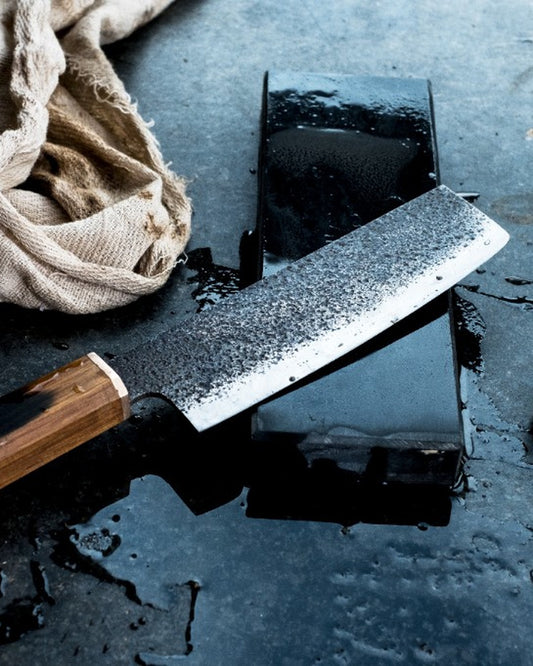 Japanese-style knife on a whetstone with water droplets — sharpening ritual