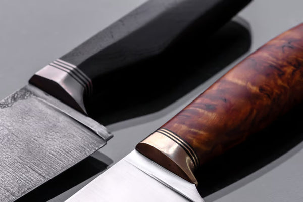 A Damascus-patterned chef's knife resting on a dark slate surface beside a halved butternut squash, soft window light revealing the wavy steel grain.