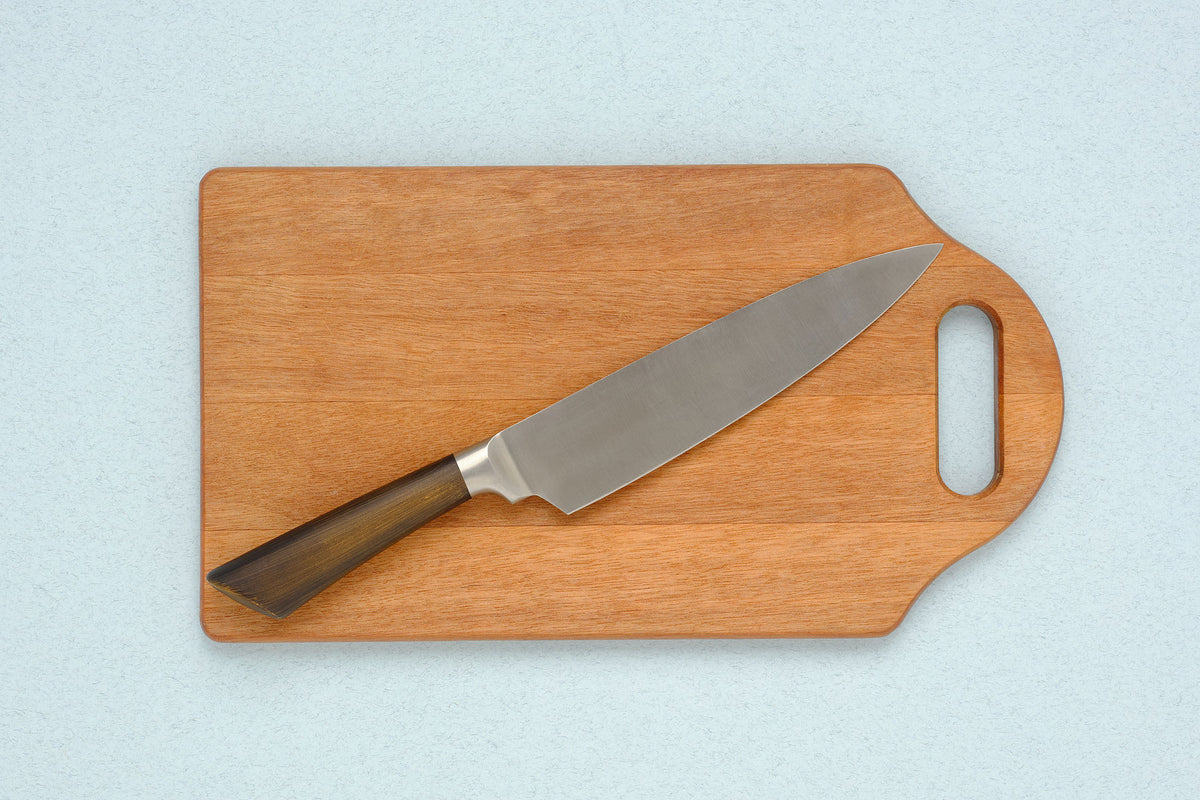 walnut cutting board and gift-boxed santoku knife on linen tablecloth with soft natural light, editorial still life, no 