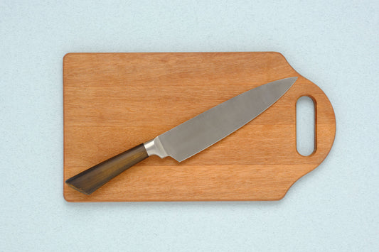 walnut cutting board and gift-boxed santoku knife on linen tablecloth with soft natural light, editorial still life, no 