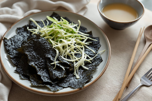 Sheets of dark nori, dried kombu strips, and pale green wakame arranged on a ceramic plate with a bowl of clear dashi, n